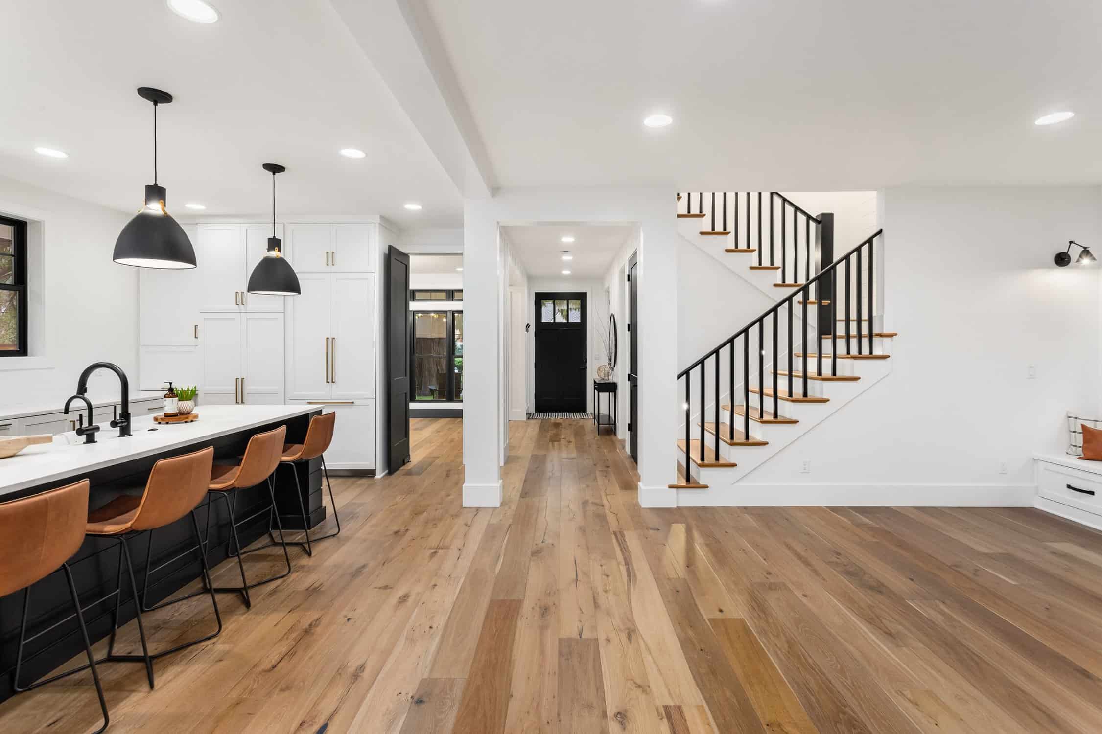 Kitchen and living room interior in new farmhouse style luxury home with open concept floor plan. Features large island with farmhouse sink, hardwood floors, and black accents. spring colors for interior