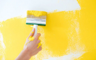 A hand painting the wall yellow